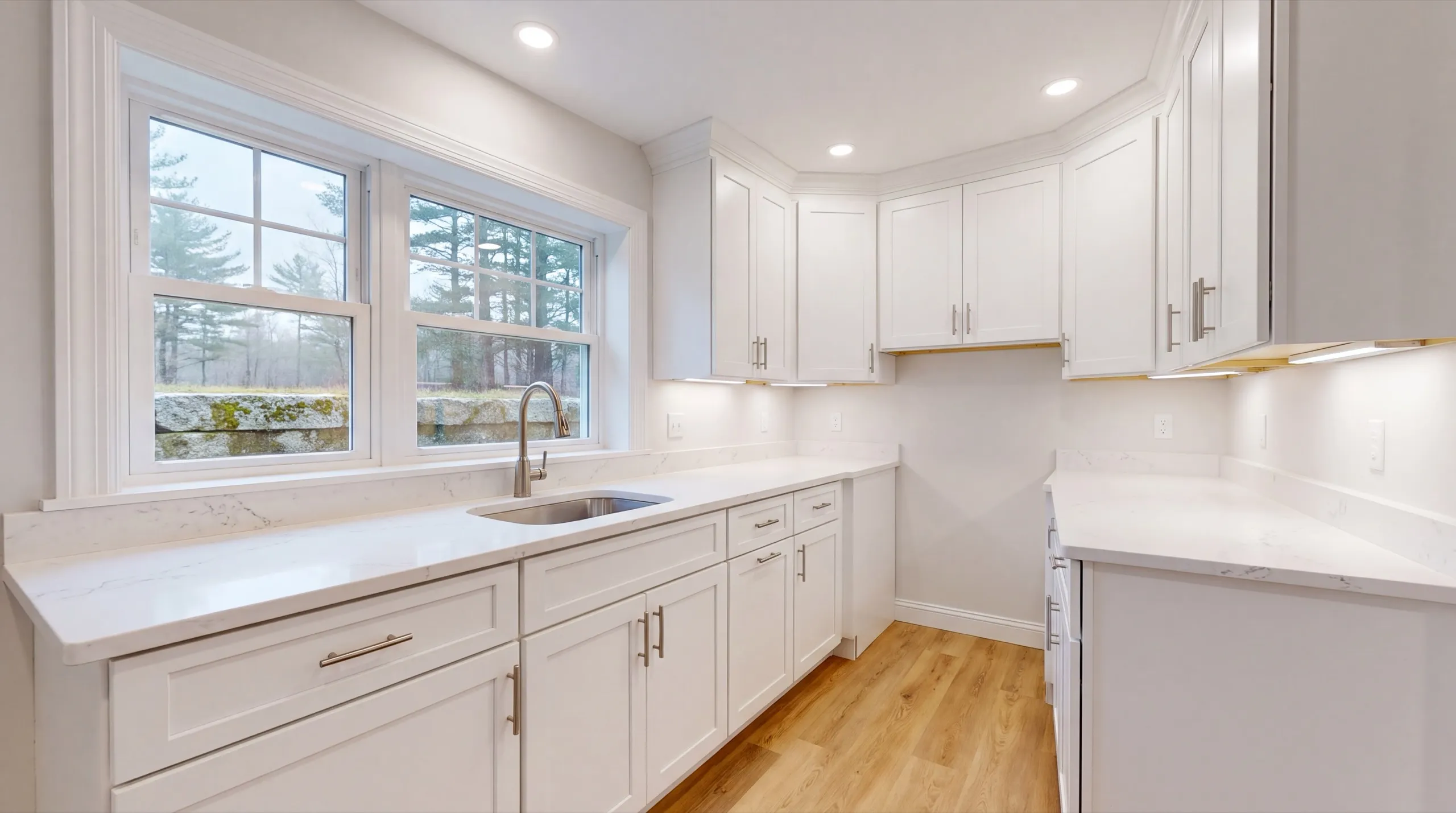 ADU builder Gardiner Maine: white kitchenette with stone counters and a sink under a double window