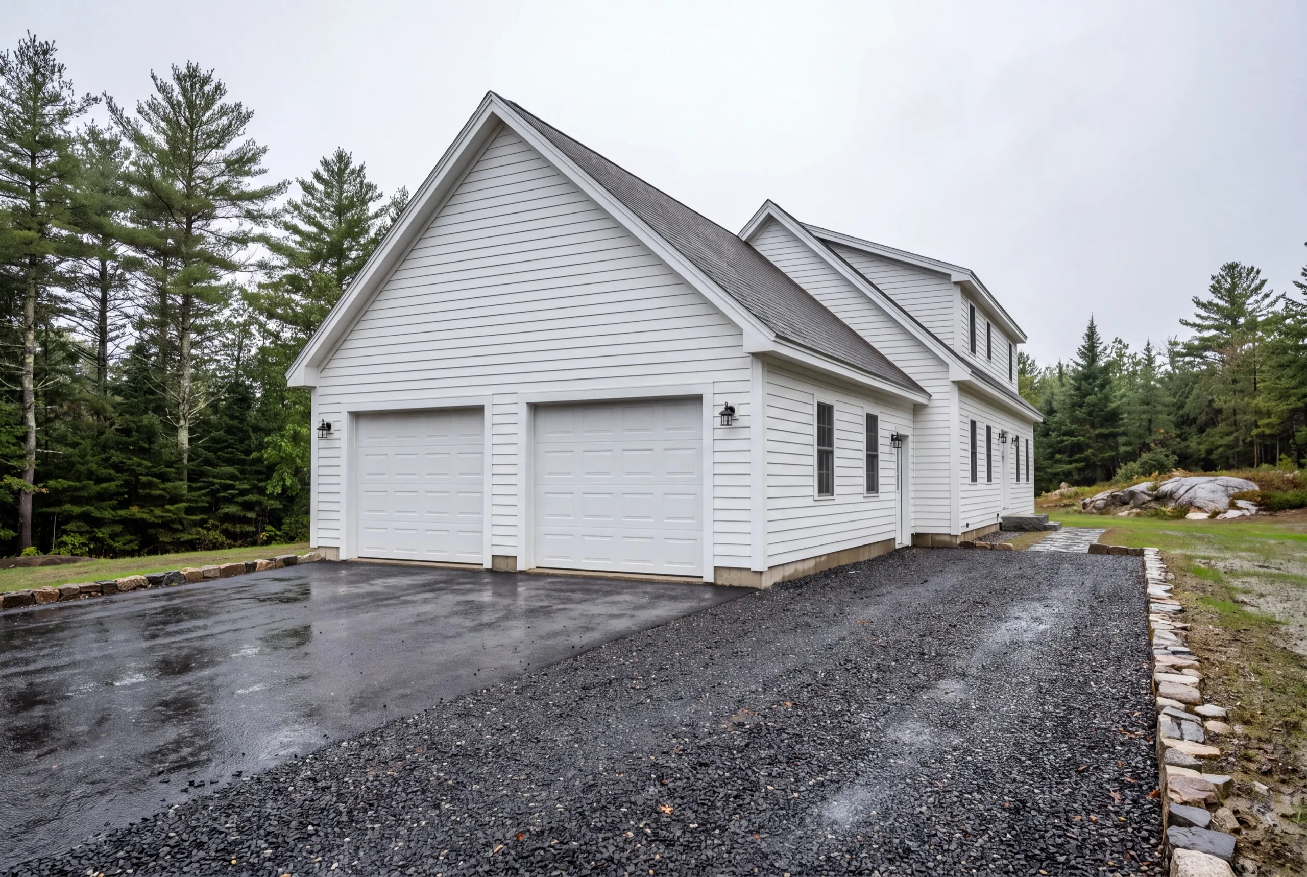 Garage builders West Gardiner Maine: white two-bay garage attached to a two-story white house on wet gravel