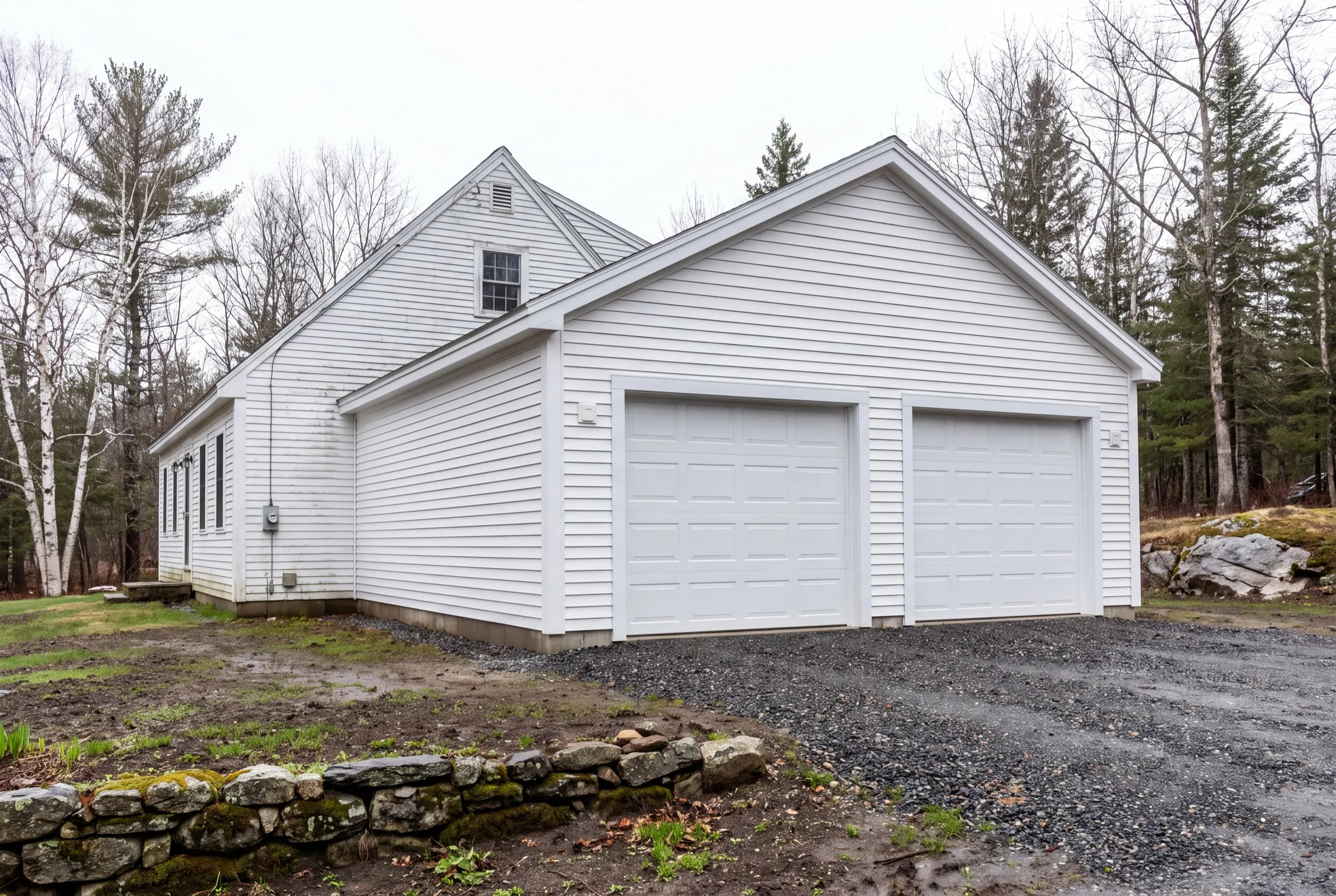 Garage builders Wiscasset Maine: white two-bay garage attached to a long white house on a gravel drive