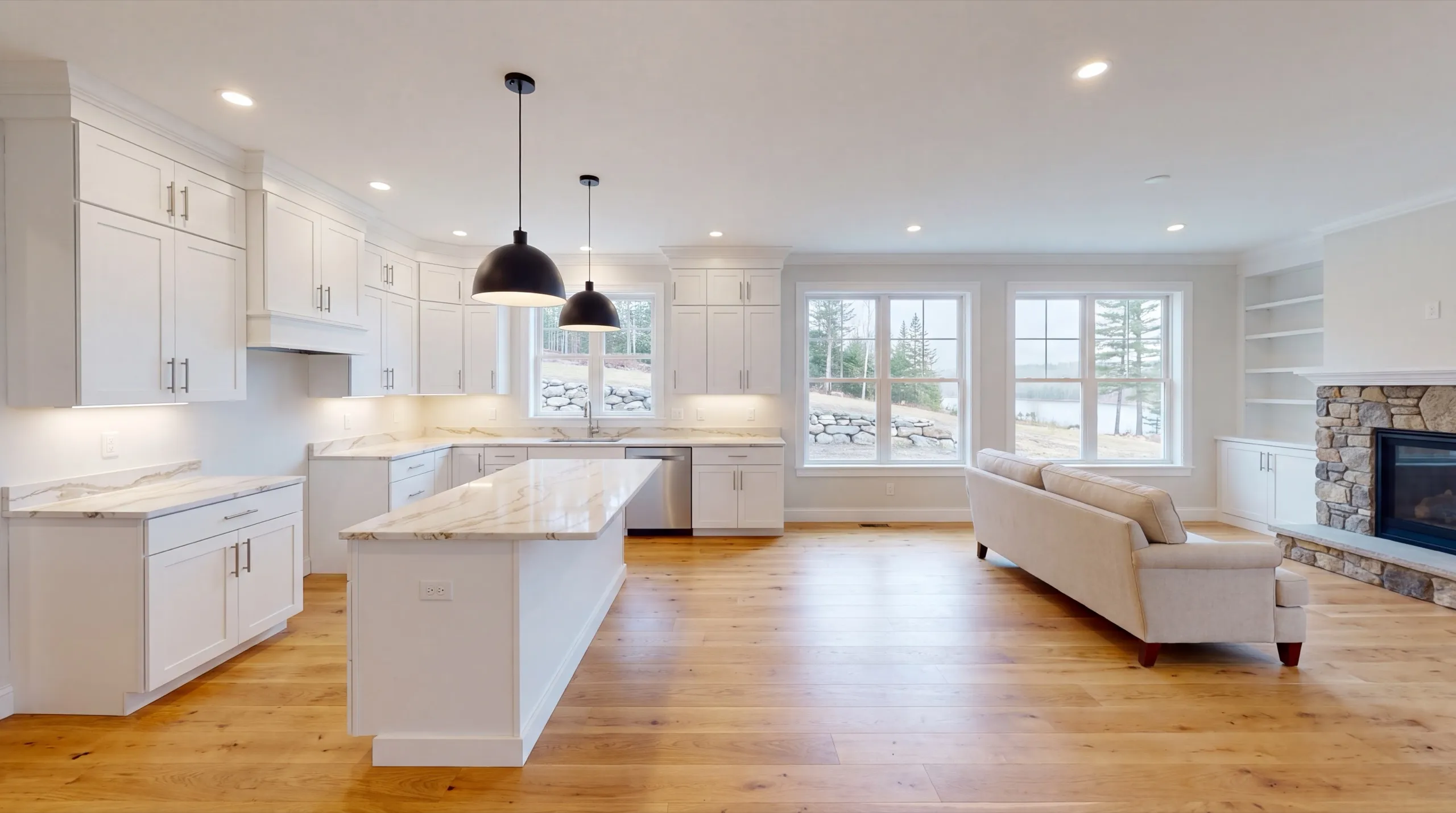 Remodeling in Pittston, ME: finished white kitchen with an island open to a living room and stone fireplace