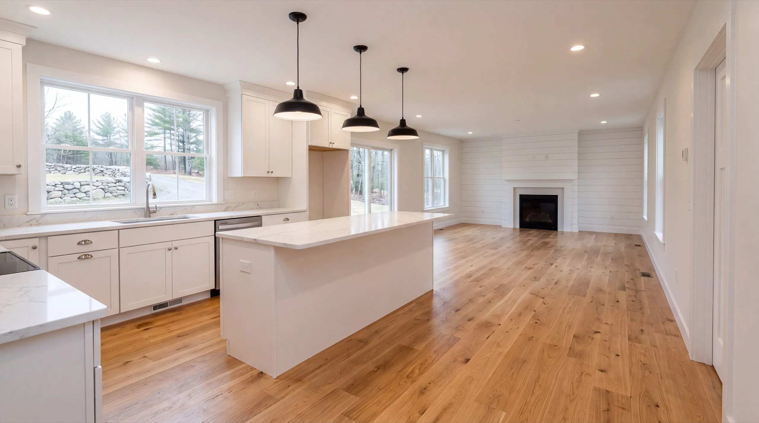 Remodeling in Vassalboro, ME: finished white kitchen with an island, black pendants and a fireplace beyond
