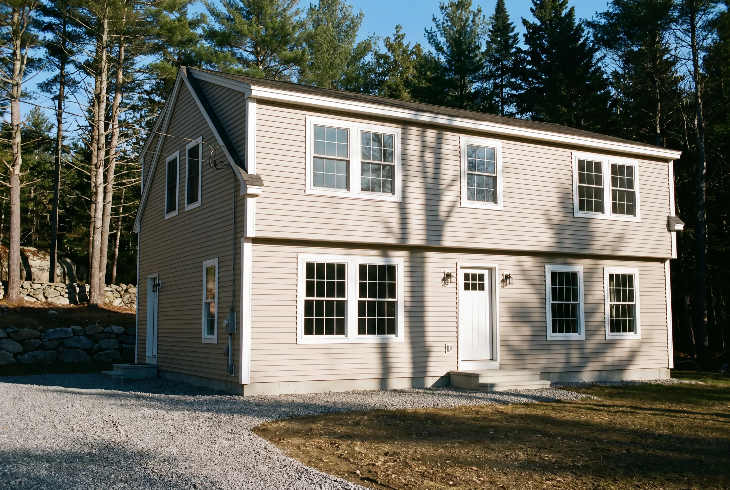 Vinyl siding contractor Dresden Maine: finished beige two-story house with vinyl siding and white trim in pine woods