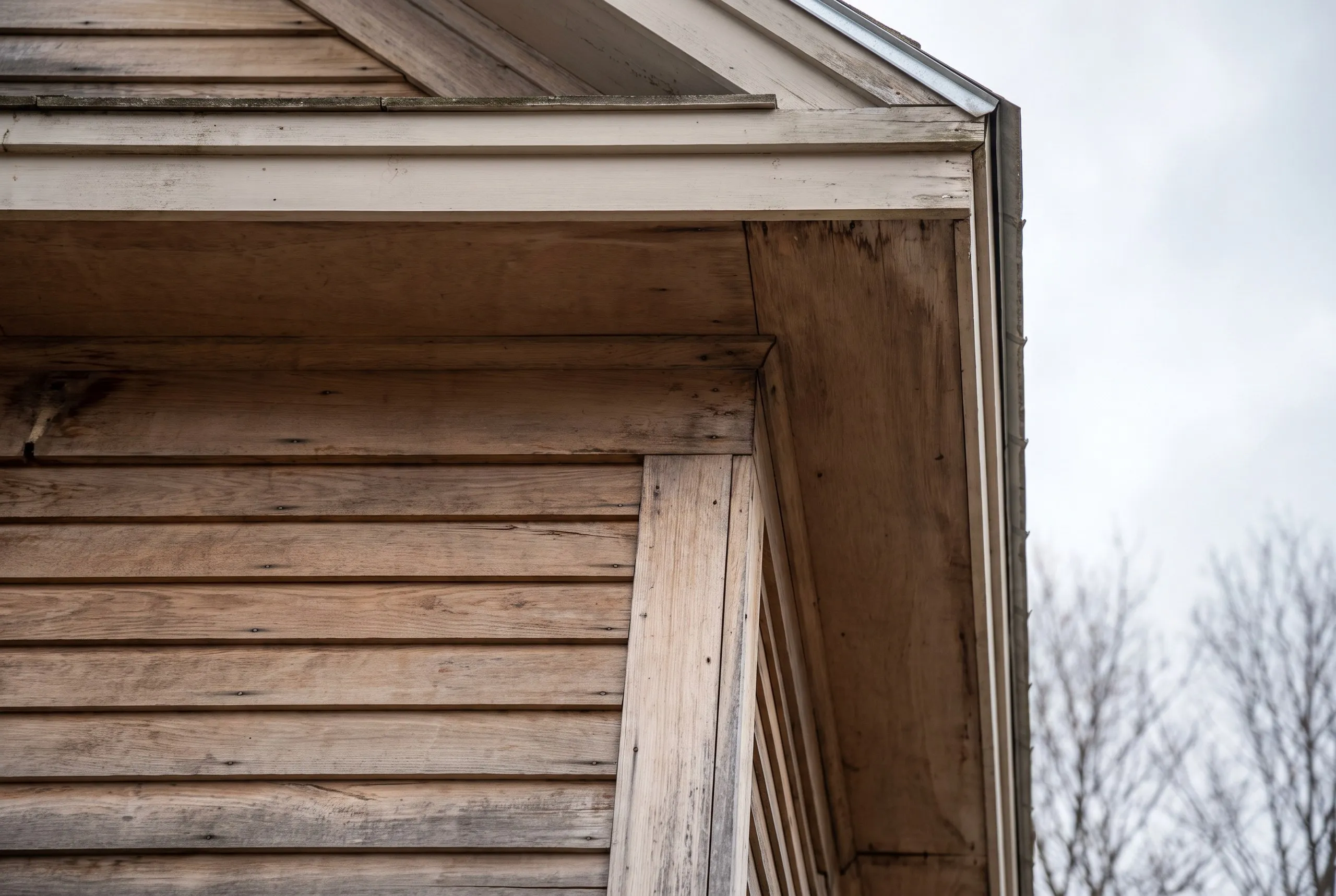 Siding installer Whitefield Maine: weathered wood lap siding, corner board and boxed eave below a gable, gutter at the edge